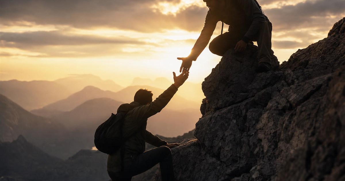 Climber at the summit, reaching a hand down to help another climber up, representing discipleship